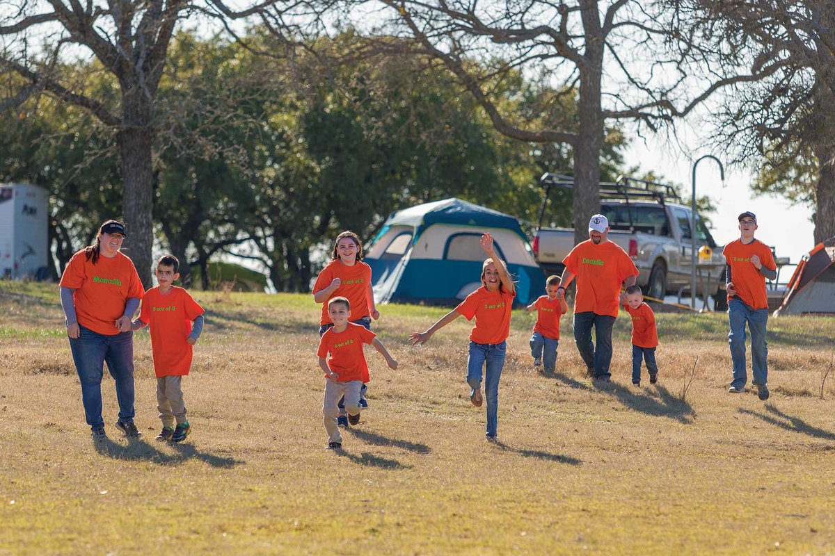 Roberto Family running down a green hill in matching orange shirts with their campsite in the background.