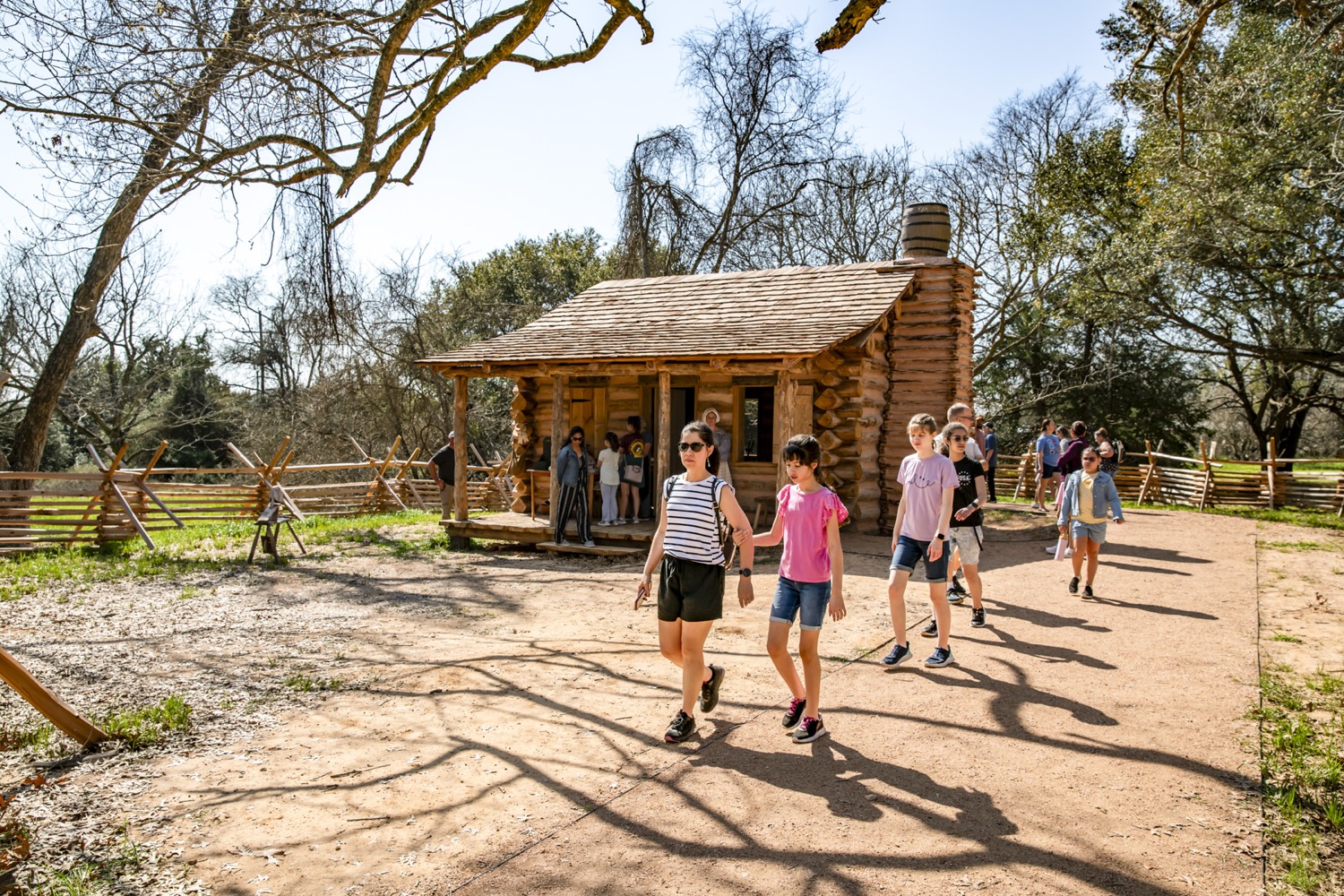 a tour group walks in front of a log cabin
