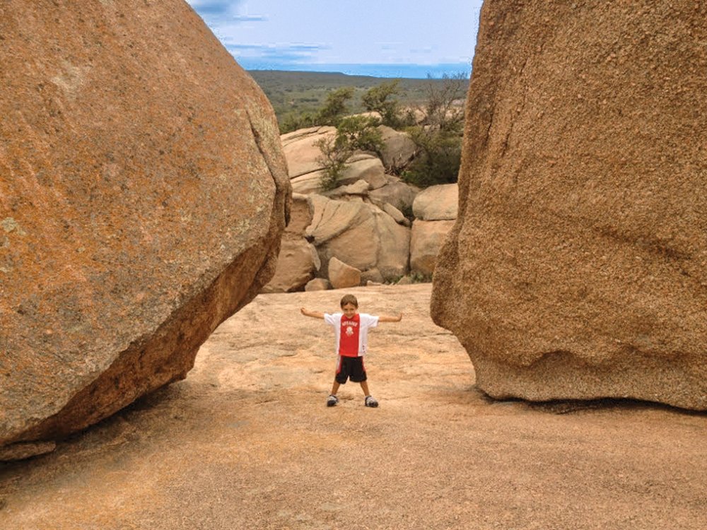 A little boy stretches out his arms between two large bolders