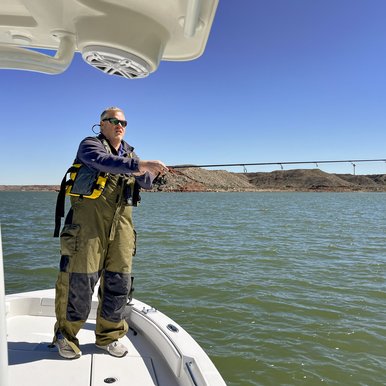 A man wearing waders fishing from a boat on the lake