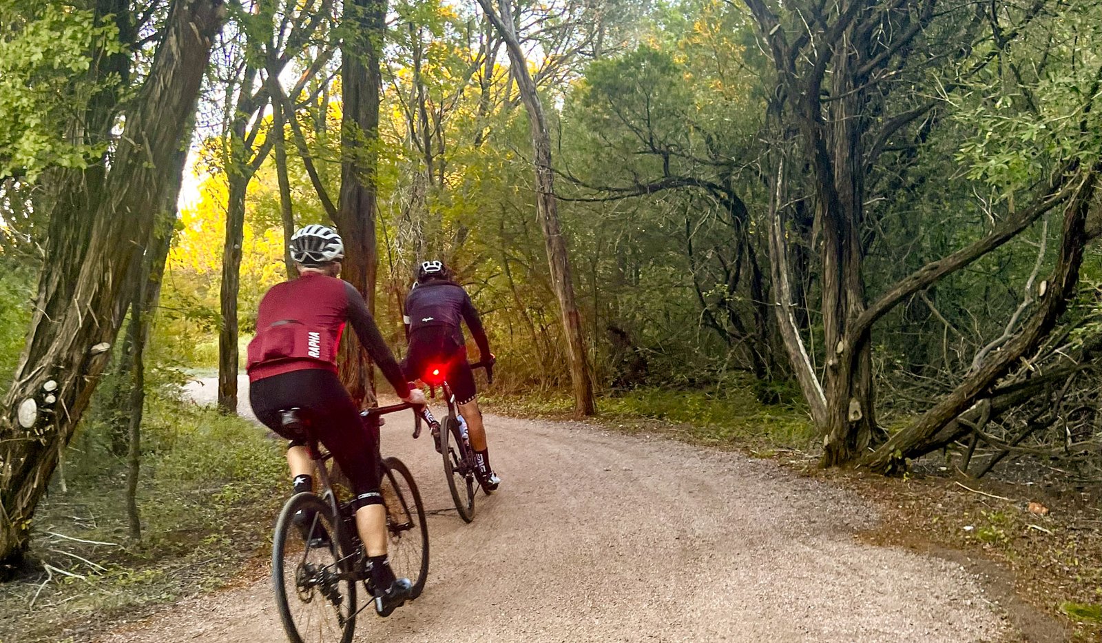 Two bikers on dirt trail surrounded by trees
