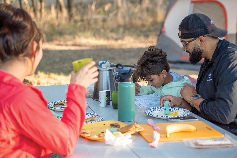 Two adults and a child sitting at a picnic table after finishing a meal. the child is looking at a map.