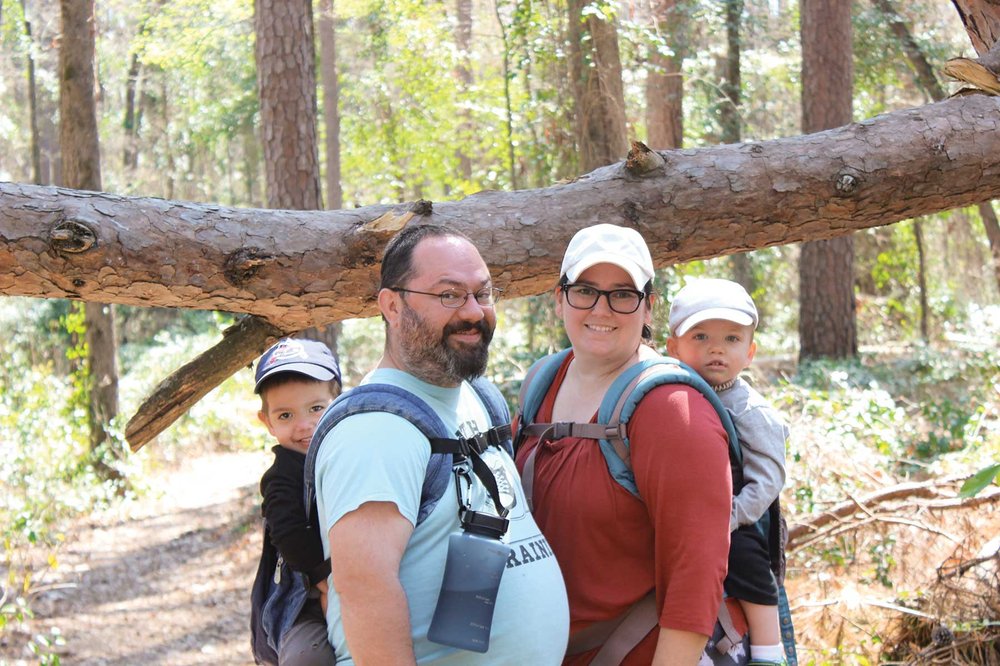 Roberto Family with babies in carriers on their back looking at the camera with a large fallen limb in the background.