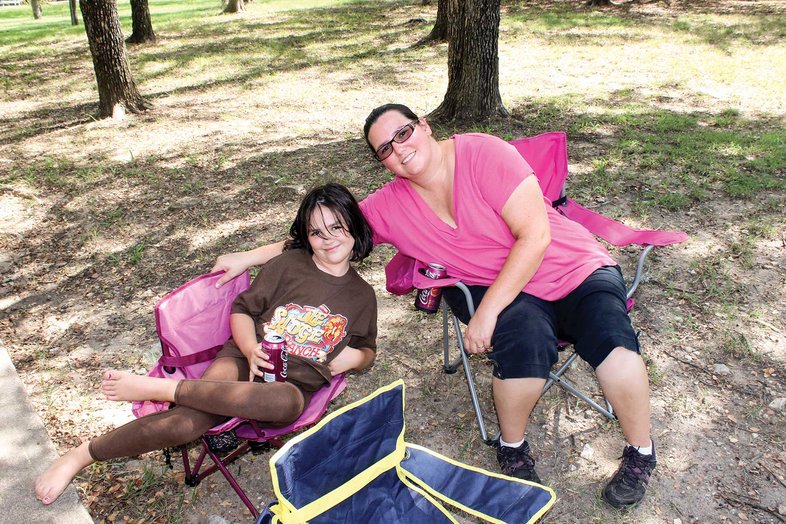 Mom in a pink shirt with girl dressed in brown sitting in camp chairs at the campsite smiling for the pictures.